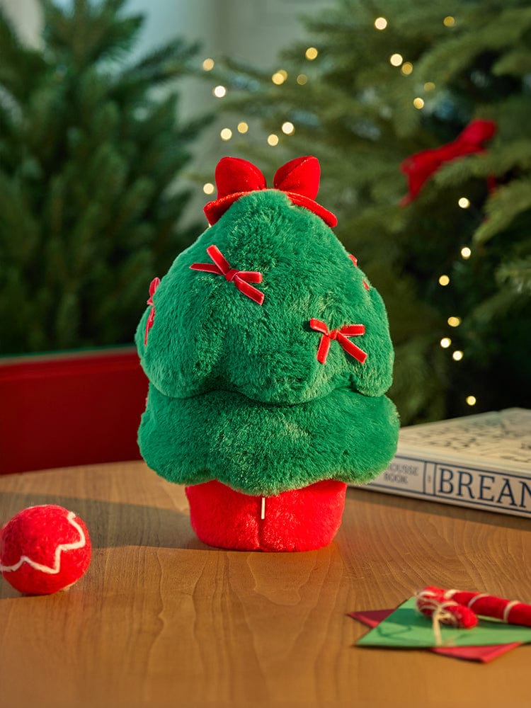 BT21 TATA minini TREE PLUSH PETITE HOLIDAY, peluche verte TATA sur table avec sapin et lumières, décor vacances.