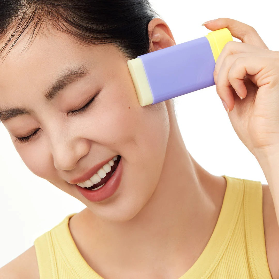 BY WISHTREND Pore Smoothing Bakuchoil Sun Stick 18g, main applique un stick solaire sur le visage, fond clair