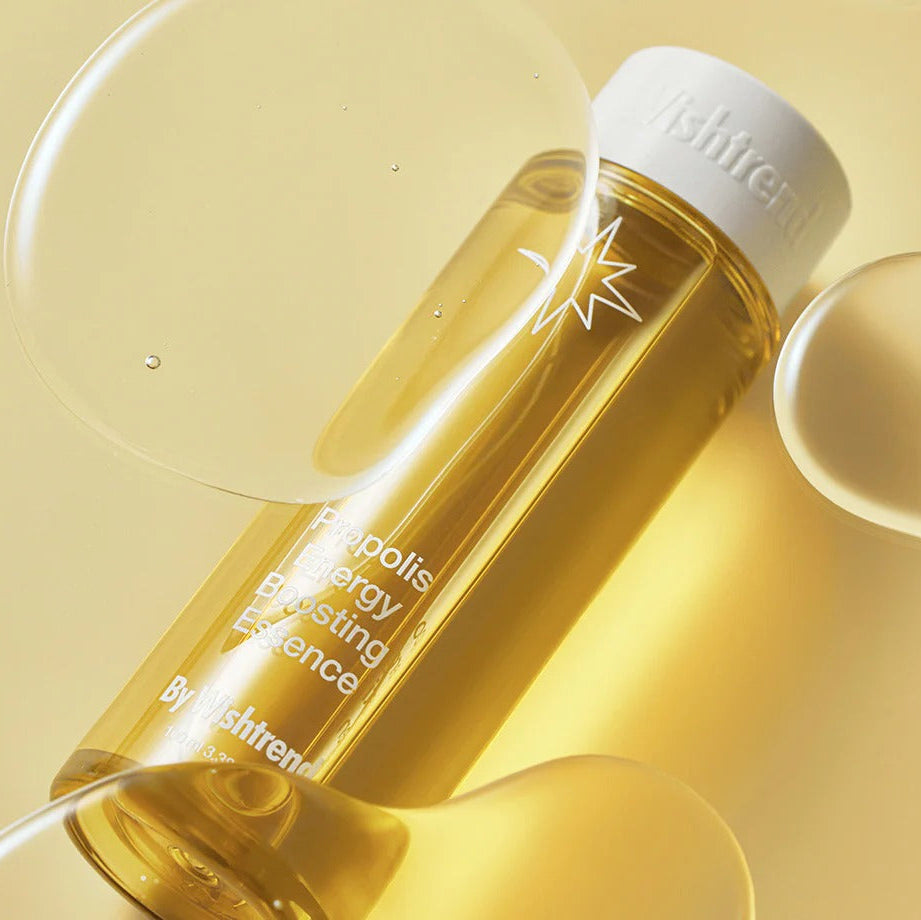 BY WISHTREND Propolis Energy Boosting Essence 100ml, flacon doré sur fond beige, gouttes et ambiance skincare.