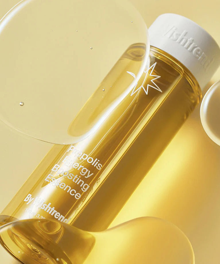 Flacon de BY WISHTREND Propolis Energy Boosting Essence 100ml sur fond doré avec des bulles, soin énergétique et revitalisant.