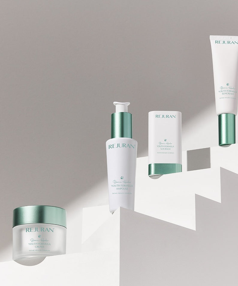 Ensemble de produits REJURAN, y compris le REJURAN Biome Healer Touth Formula Sunscreen 50ml, en présentation minimaliste.