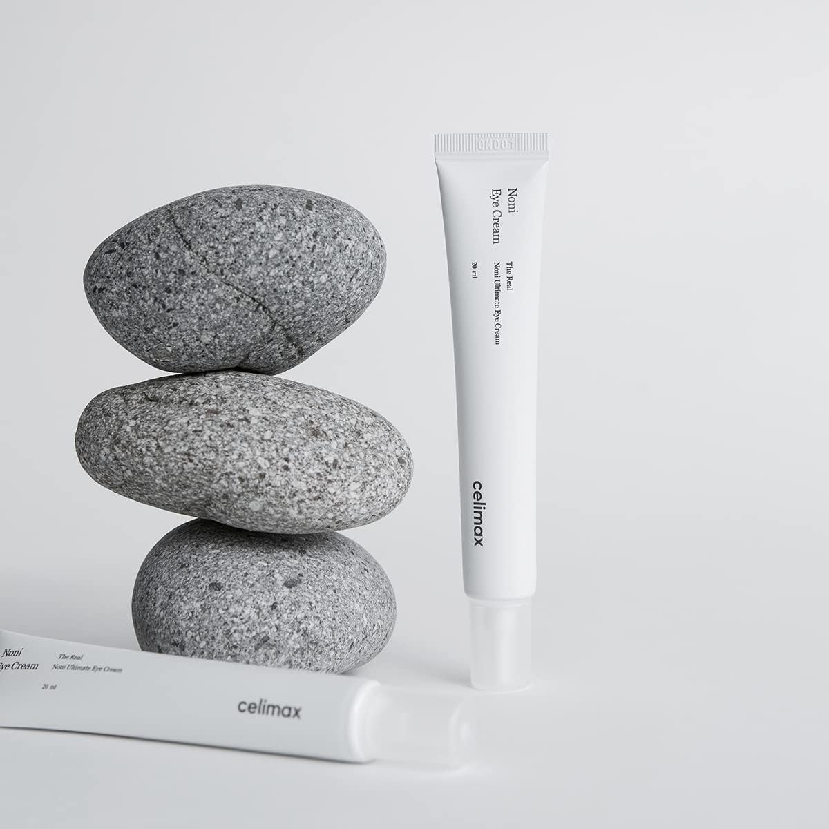 CELIMAX The Real Noni Ultimate Eye Cream 20ml, tube blanc sur pierres grises, fond blanc, produit de marque Celimax