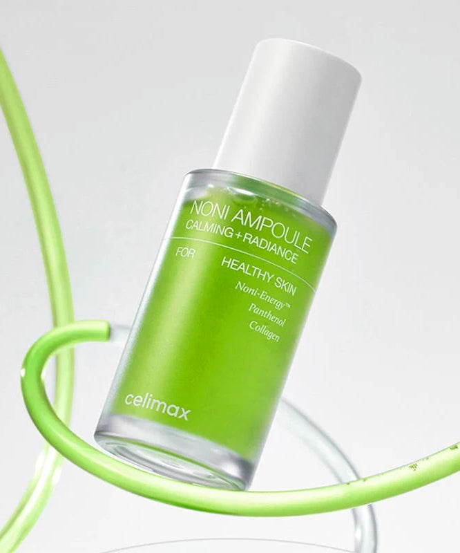 Flacon vert de CELIMAX Noni Ampoule Calming+Radiance 30ml posé sur un support moderne.