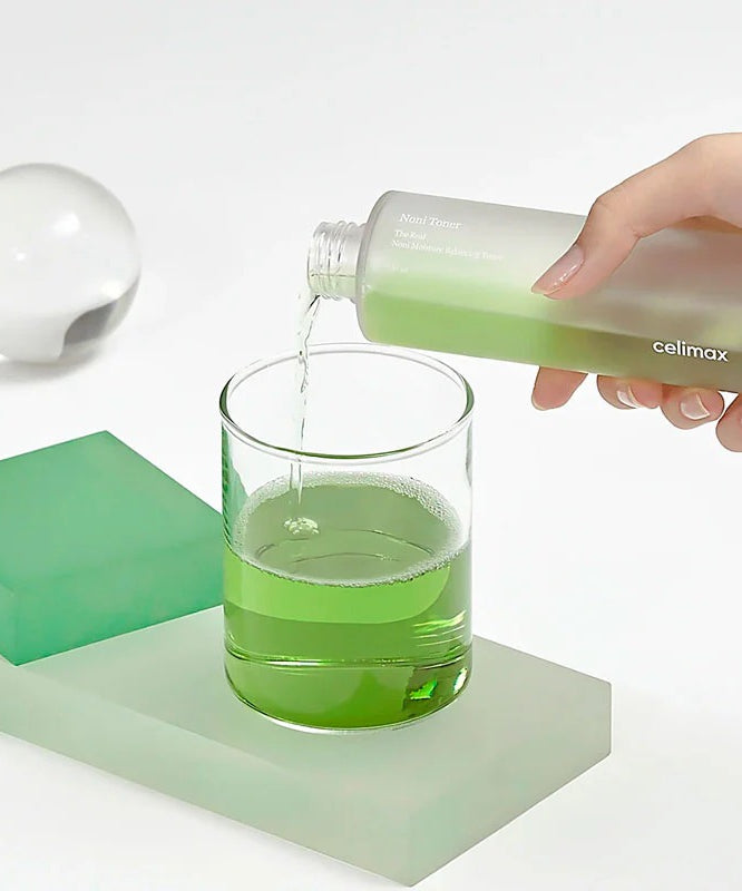 Versement de CELIMAX The Real Noni Moisture Balancing Toner 320ml dans un verre pour une hydratation équilibrée en profondeur.