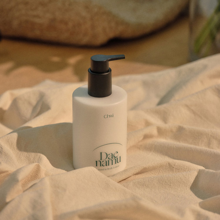 CHWI (CHI) Dae Namu Hand & Body Lotion 300ml de CHWI, flacon sur linge beige, contexte spa chaleureux, lumière douce