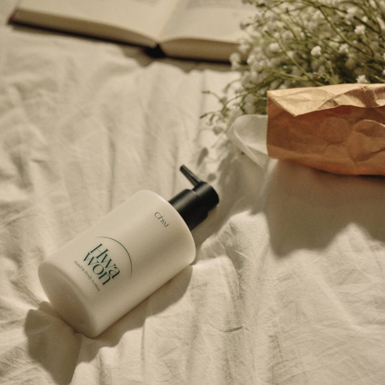 CHWI (CHI) Hwa Won Hand & Body Lotion 300ml, bouteille sur drap beige avec fleurs et livre, contexte détente à la maison