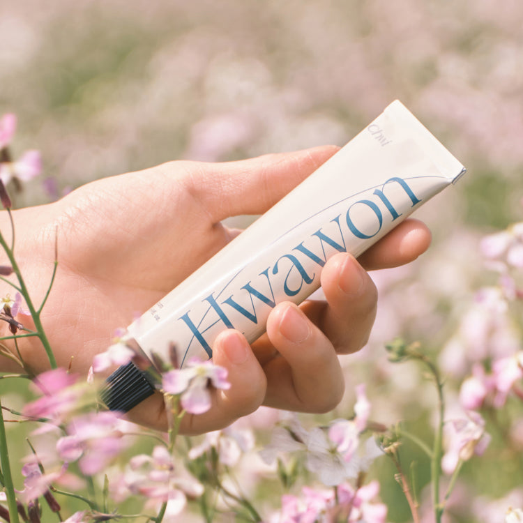 Main tenant CHWI (CHI) Hwa Won Hand Cream 50ml dans un champ de fleurs, crème mains de la marque CHWI (CHI).