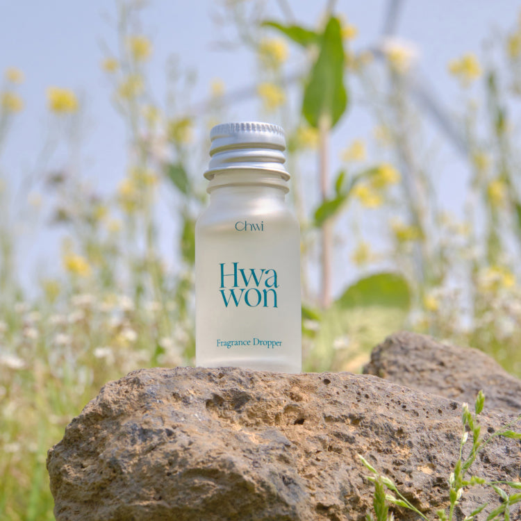 CHWI (CHI) Wha Won Fragrance Dropper 10ml, flacon marque Chwi, en extérieur sur pierre, fleurs jaunes floues en arrière-plan.