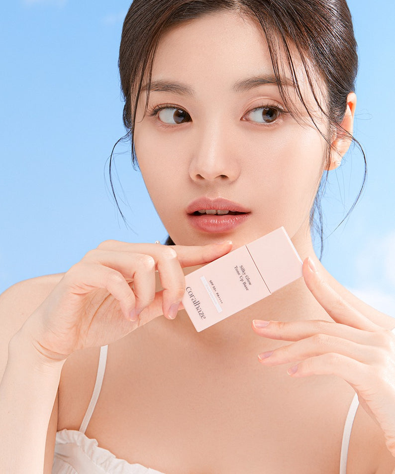 Femme tenant le CORALHAZE SIlky Glow Tone Up Base devant un ciel bleu.