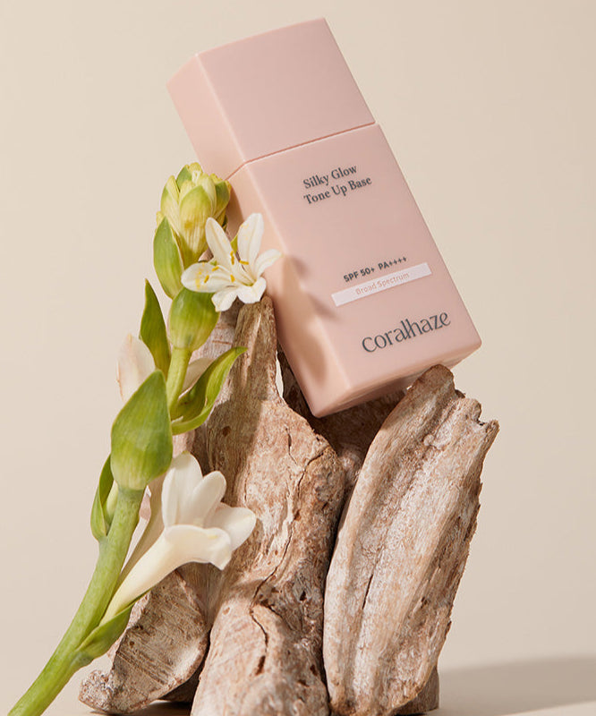 CORALHAZE SIlky Glow Tone Up Base présenté sur un fond naturel avec des fleurs délicates, accentuant son esthétique élégante.
