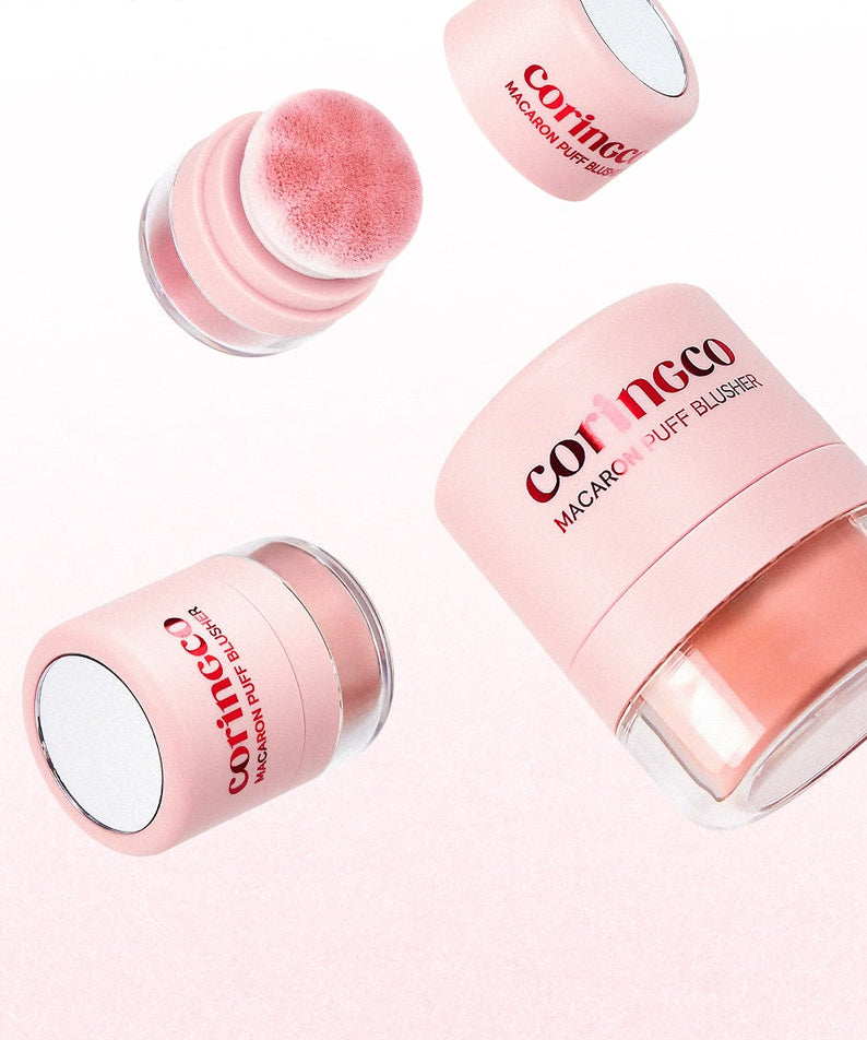 Décris l'image en français : CORINGCO Macaron Puff Blusher, produits CORINGCO rose maquillage, poudres et bouchon sur fond clair.