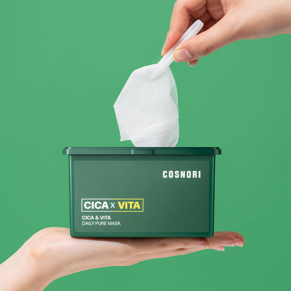 Main tenant COSNORI Cica & Vita Daily Pure Mask 30 sheets, sachet de masques sur fond vert, boîte COSNORI visible.