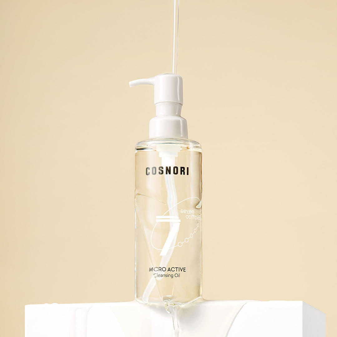 COSNORI Micro Active Cleansing Oil 200ml de la marque COSNORI, flacon pompe sur fond beige avec éclaboussures d’huile