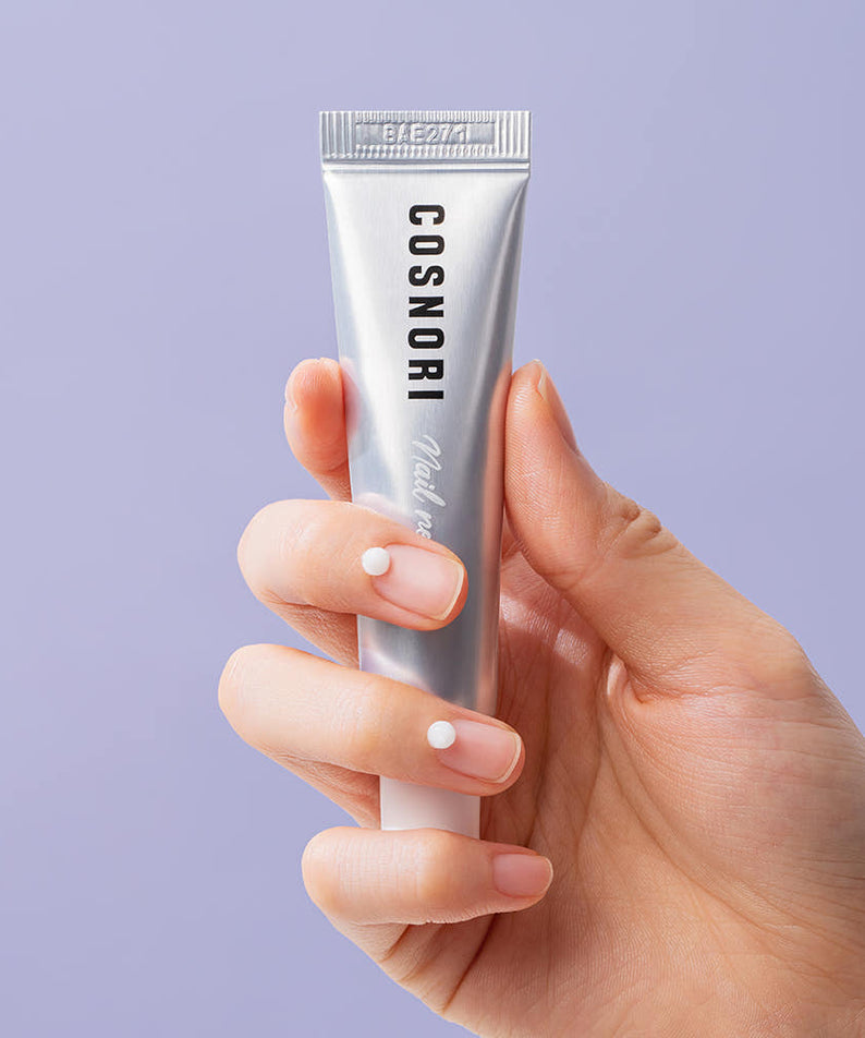 Main tenant COSNORI Nail Nutrition Silk Repair Nail Cream 15ml 2ea, crème de réparation des ongles sur fond clair.