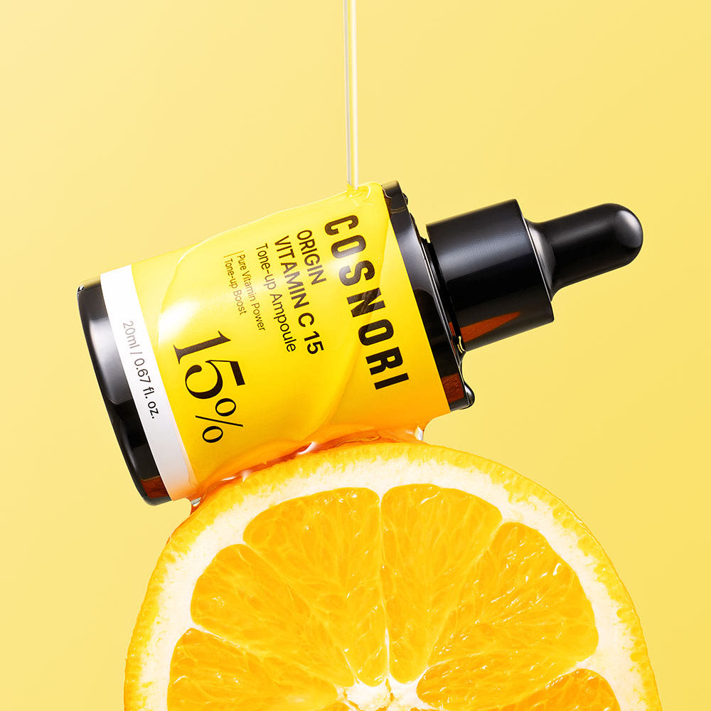 COSNORI Origin Vitamin C 15 Tone-Up Ampoule 20ml de la marque COSNORI, sur fond jaune, avec oranges tranchées.