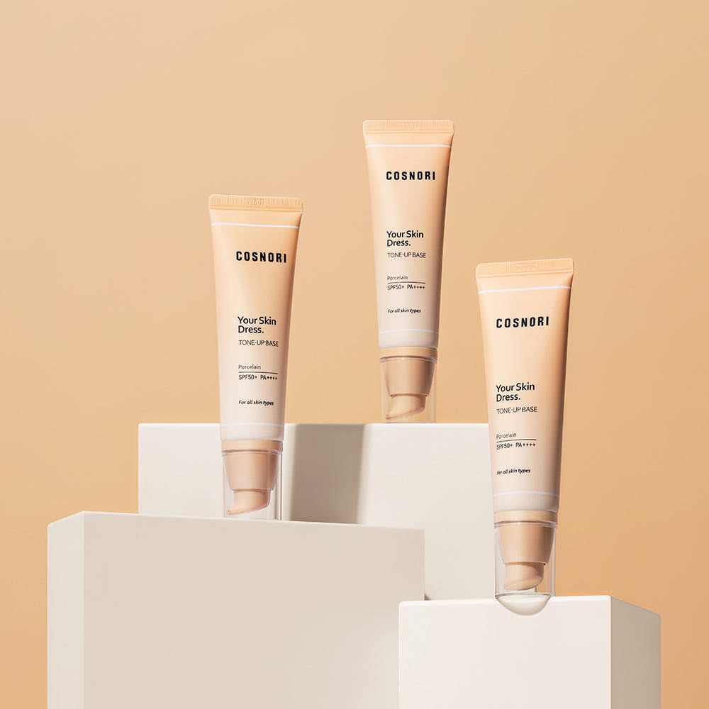COSNORI Your Skin Dress Tone-Up Base 50ml de COSNORI, tubes cosmétiques sur socles blancs, fond beige.