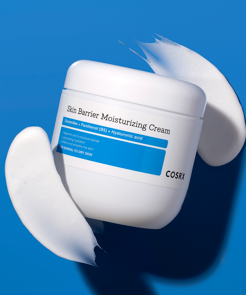 COSRX Skin Barrier Moisturizing Cream 450ml, pot de crème cosmétique blanc sur fond bleu, texture de crème en éclaboussures