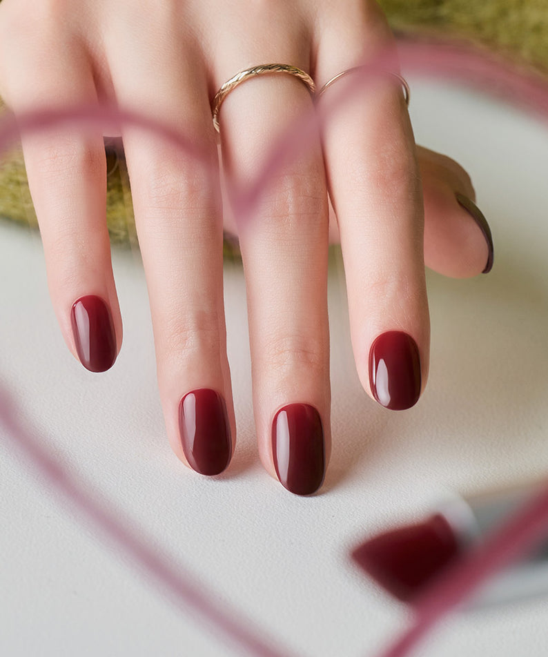 DASHING DIVA  Classic Burgundy (Oval) sur ongles, main tenant une pochette, marque Dashing DIVA, fond clair extérieur