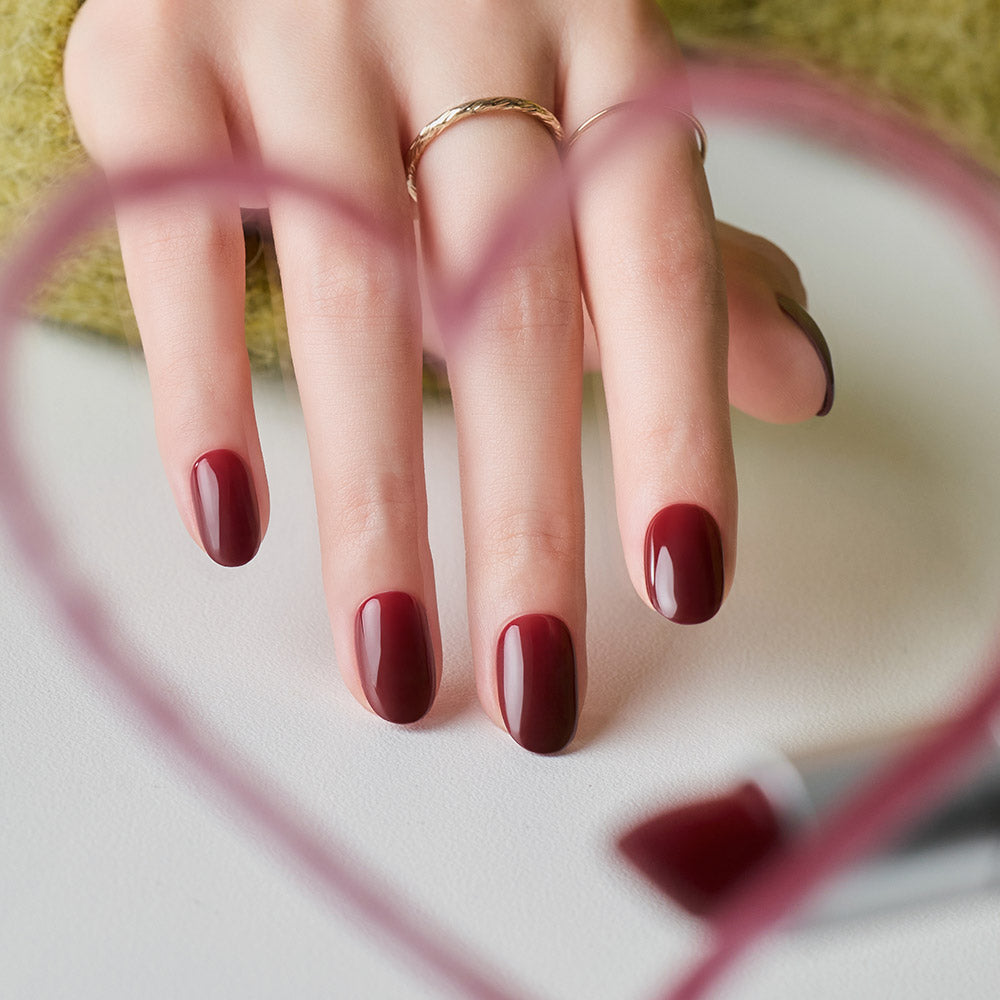 DASHING DIVA  Classic Burgundy (Oval) sur ongles, main tenant une pochette, marque Dashing DIVA, fond clair extérieur