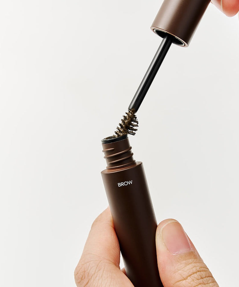 DASHU Daily Dual Hair Cover Mascara de la marque DASHU : applicateur près du tube brun, main maquillant les sourcils.
