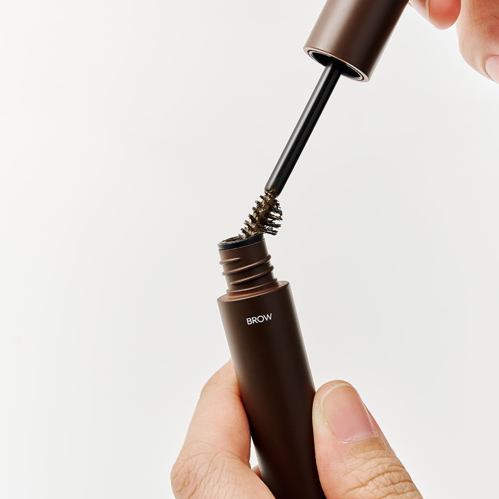 DASHU Daily Dual Hair Cover Mascara de la marque DASHU : applicateur près du tube brun, main maquillant les sourcils.