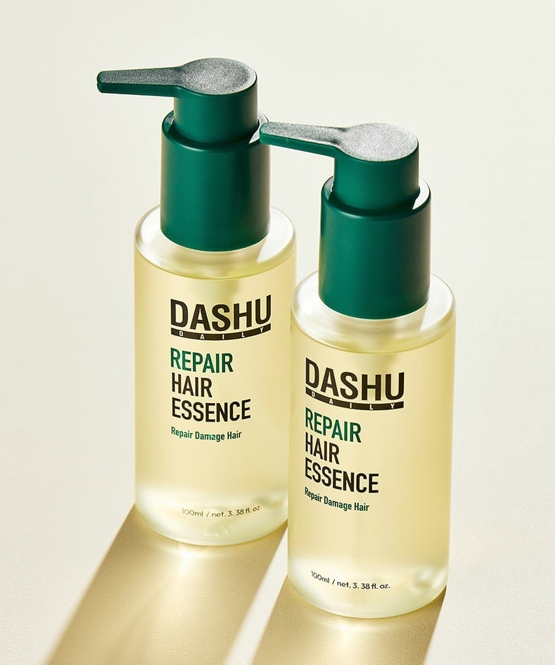 Deux flacons de DASHU Daily Repair Hair Essence 100ml posés sur une surface beige, offrant un soin réparateur pour cheveux abîmés.