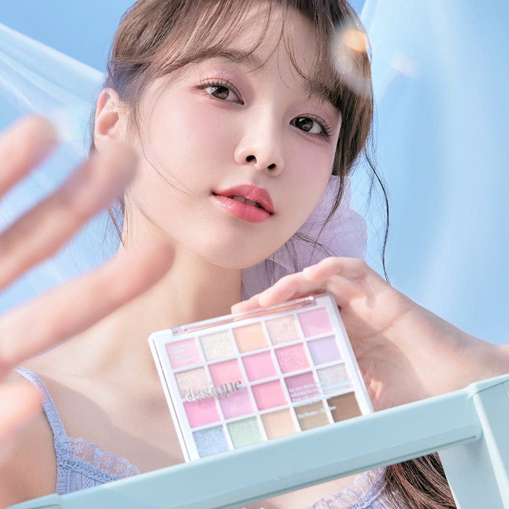 Portrait maquillage : DASIQUE Mood Shadow Palette (#01 to #07) sur un miroir, palette yeux avec couleurs pastel, fond bleu.