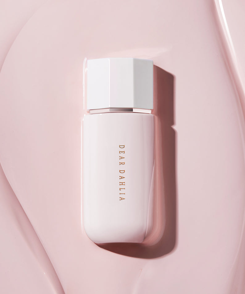 Prime Layer Glow Primer de DEAR DAHLIA sur fond rose élégant, produit de beauté luxueux pour une peau radieuse et éclatante.