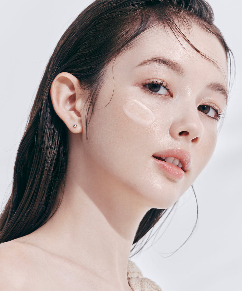 Femme appliquant DEAR DAHLIA Prime Layer Skin Prep sur visage, produit de soin beauté pour peau éclatante et hydratée.