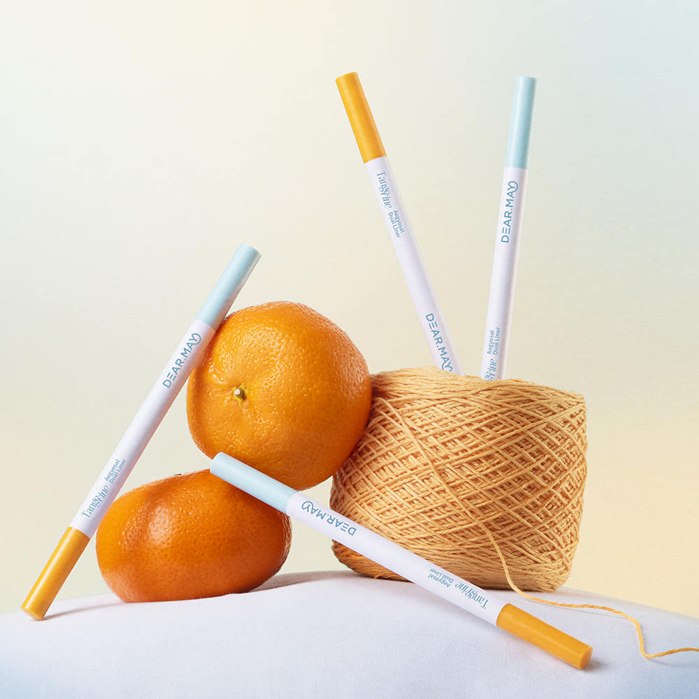 DEAR MAY Tangerine Aegyo-sal Dual Liner de la marque DEAR MAY, stylos maquillage près d’oranges et de filet à la lumière.