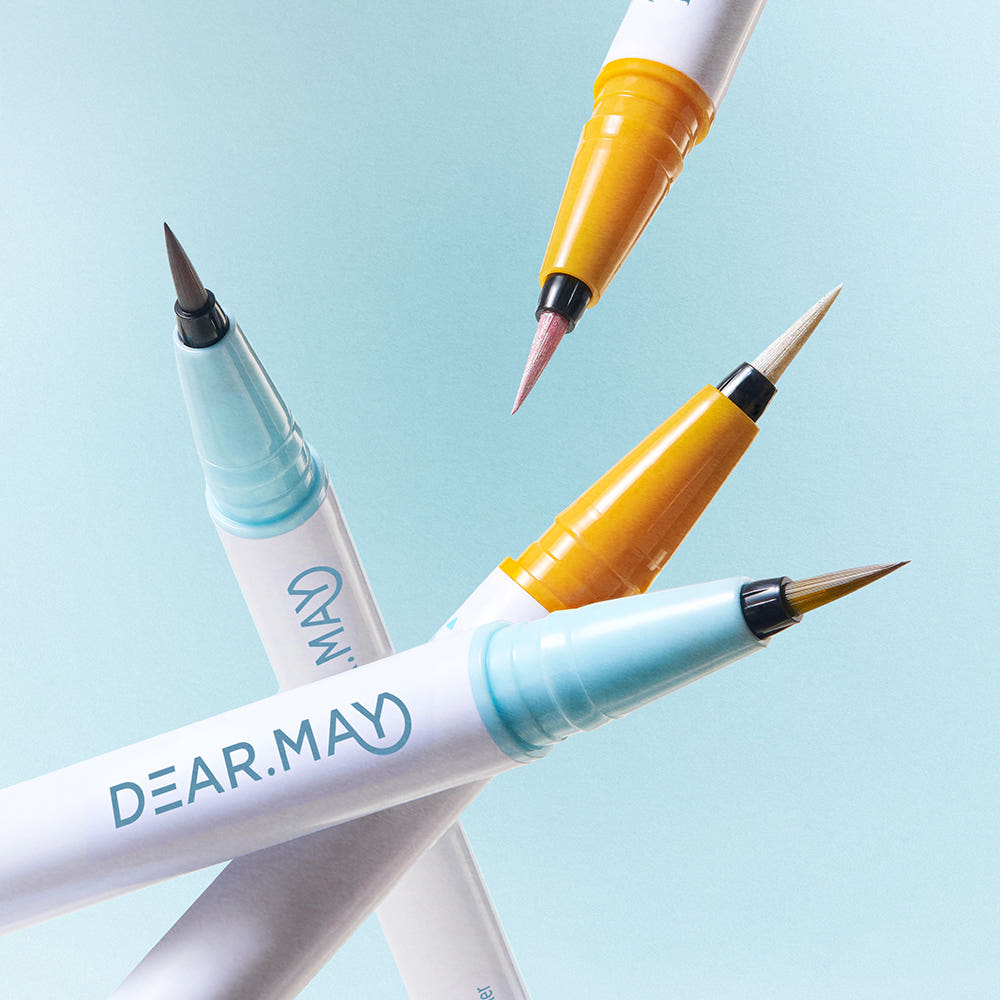 DEAR MAY Tangerine Aegyo-sal Dual Liner de la marque DEAR MAY, stylos yeux double embout avec tons orange sur fond bleu clair.
