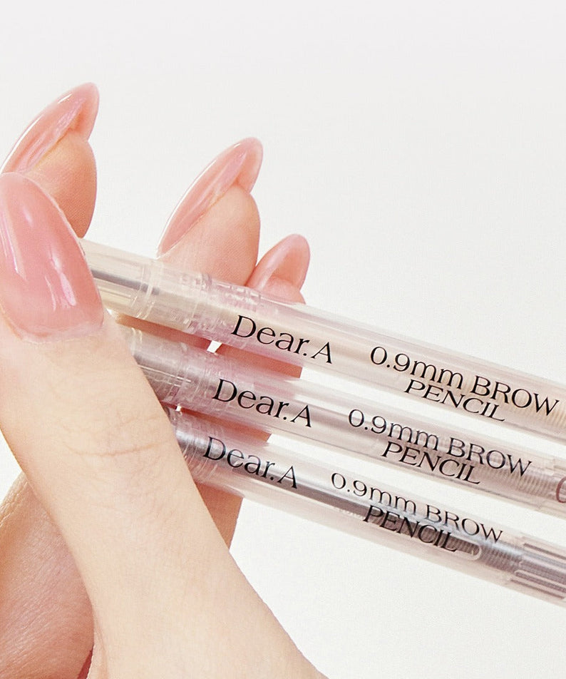 Main tenant DEAR.A 0.9mm Eyebrow, stylo anti-cernes, marques lisibles sur produit transparent, fond clair.
