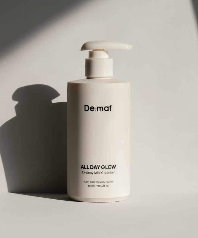 DE:MAF All Day Glow Creamy Milk Cleanser 300ml de De:mat, flacon blanc sur fond clair, lumière studio.