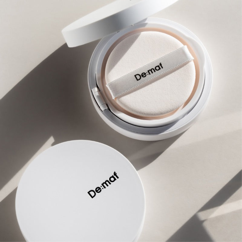 DE:MAF Bora Blossom Tone-Up Cushion De:maf en coussin tonifiant, packaging ouvert, lumière naturelle sur fond clair.