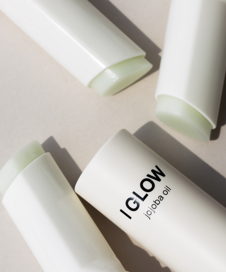 Décris l'image en français : DE:MAF Eye Glow Jojoba Oil Multi Balm 9g, baume vert à l’huile de jojoba, sur fond clair.
