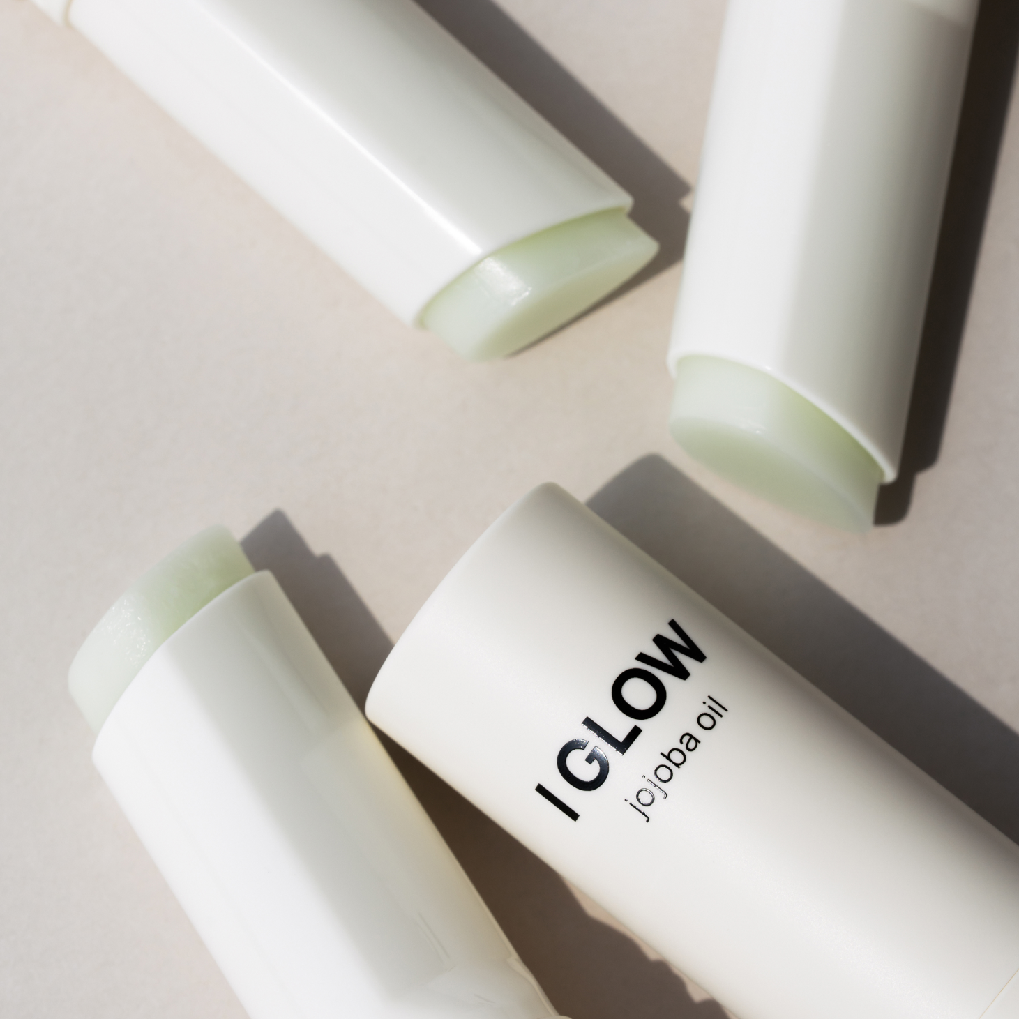 Décris l'image en français : DE:MAF Eye Glow Jojoba Oil Multi Balm 9g, baume vert à l’huile de jojoba, sur fond clair.