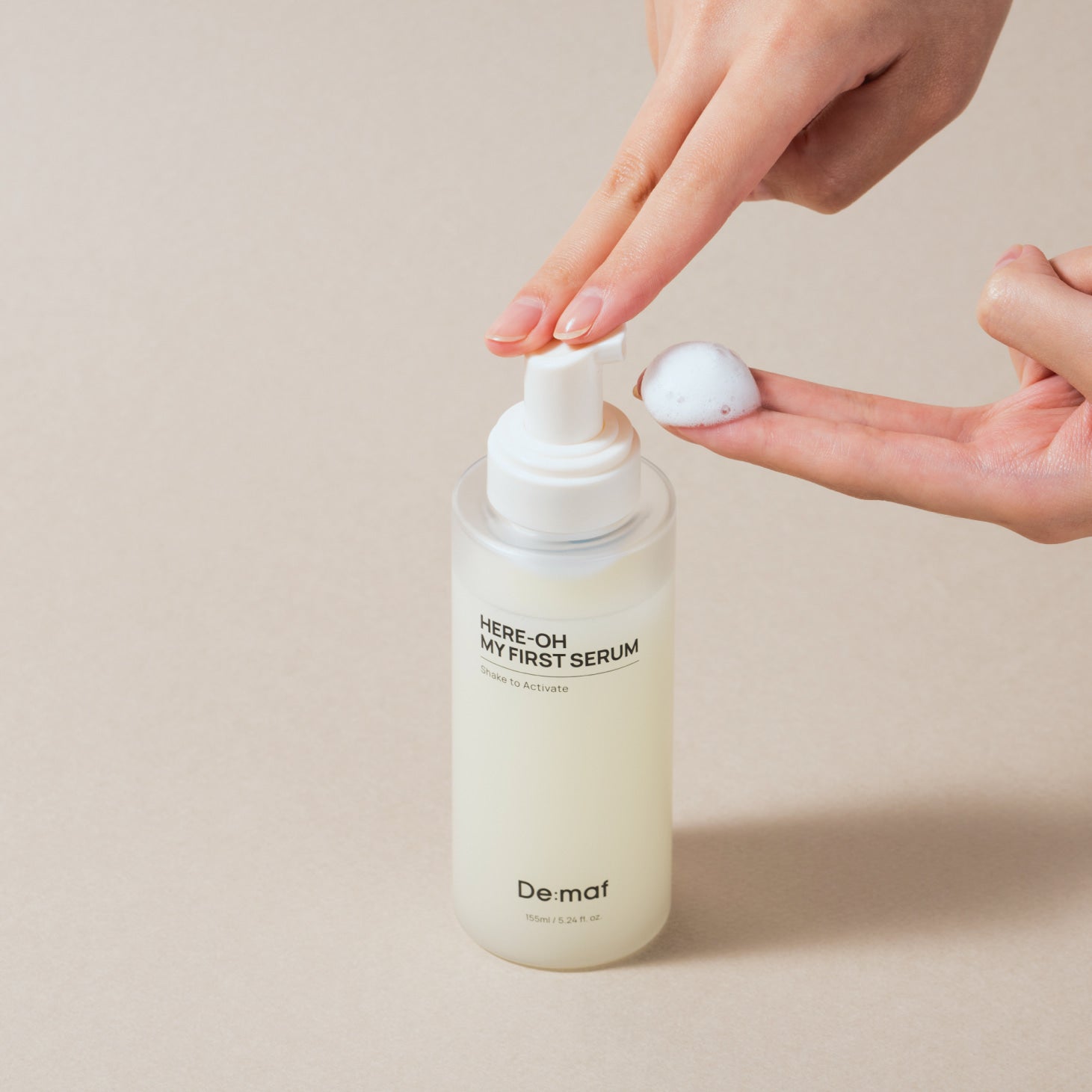 DE:MAF Here-Oh My First Serum 155ml, main ouvrant une pompe, produit De:maf sur fond beige, contexte soin beauté.