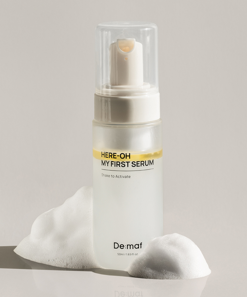 DE:MAF Here-Oh My First Serum 155ml, De maf, sérum en flacon blanc sous sur coussin, fond clair.