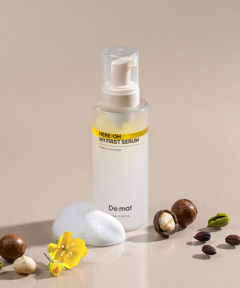 DE:MAF Here-Oh My First Serum 155ml de De:maf, flacon sérum sur fond beige, avec fleurs, pierres et feuilles.