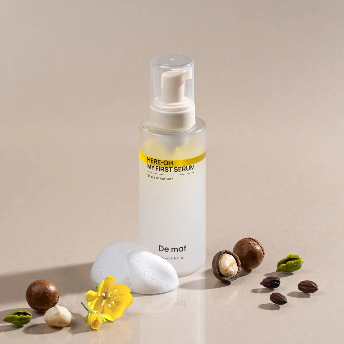 DE:MAF Here-Oh My First Serum 155ml de De:maf, flacon sérum sur fond beige, avec fleurs, pierres et feuilles.