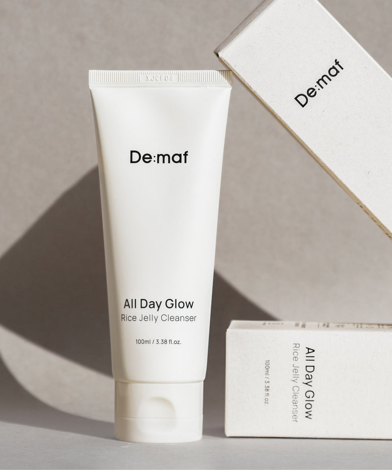 DE:MAF Rice Jelly Cleanser 100ml De:maf, tube blanc sur fond beige avec coffret en arrière-plan.