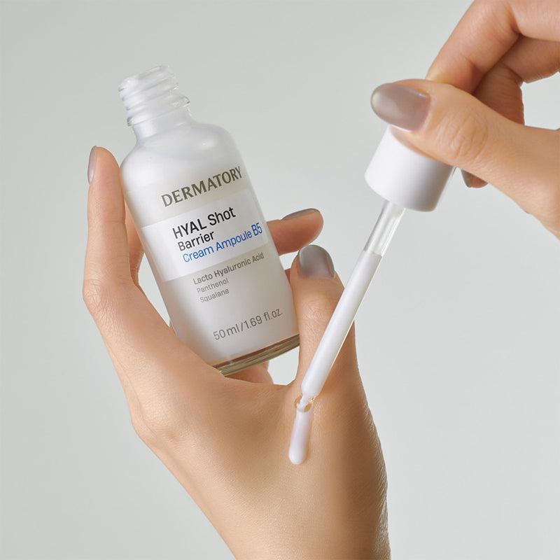 DERMATORY Hyal Shot Barrier Cream Ampoule B5 50ml, mains tenant le flacon et une pipette, fond clair, contexte cosmétique.