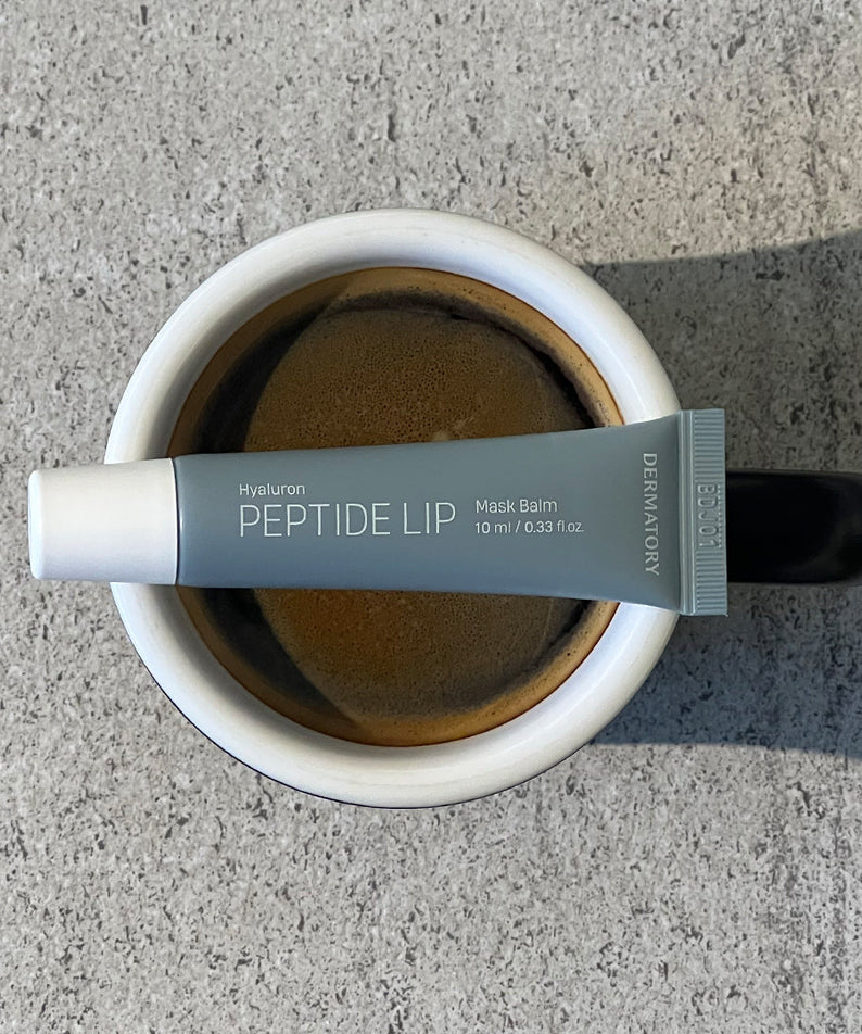 DERMATORY Hyaluronic Peptide Lip Keyring sur une tasse de café, crème anti-rides pour les lèvres sur fond béton