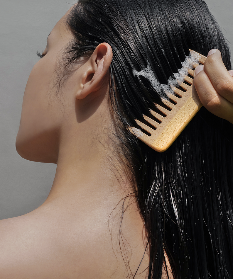 Femme utilisant le DONGGUBAT Correct Shampoo Bar For Oily Skin avec un peigne en bois pour cheveux gras brillants.