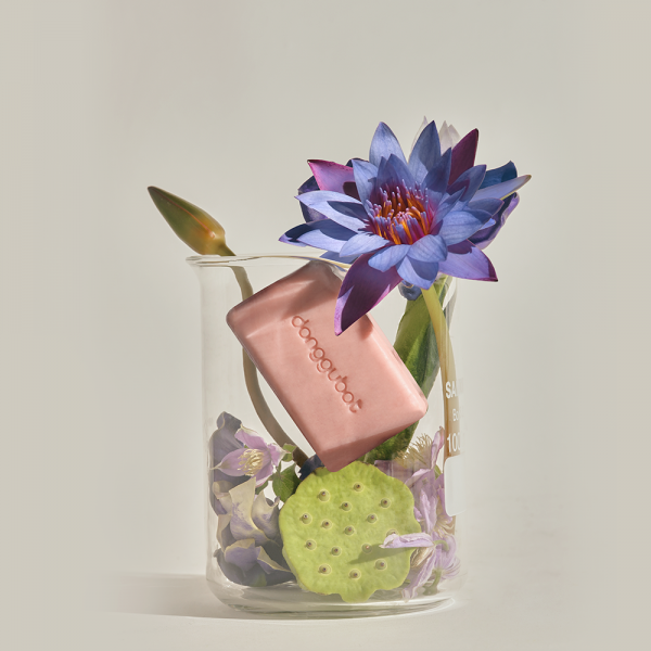 DONGGUBAT Blooming Jaungo Washing Bar 80g, savon en cube rose, marque visible, posé avec fleurs tropicales dans un bocal.