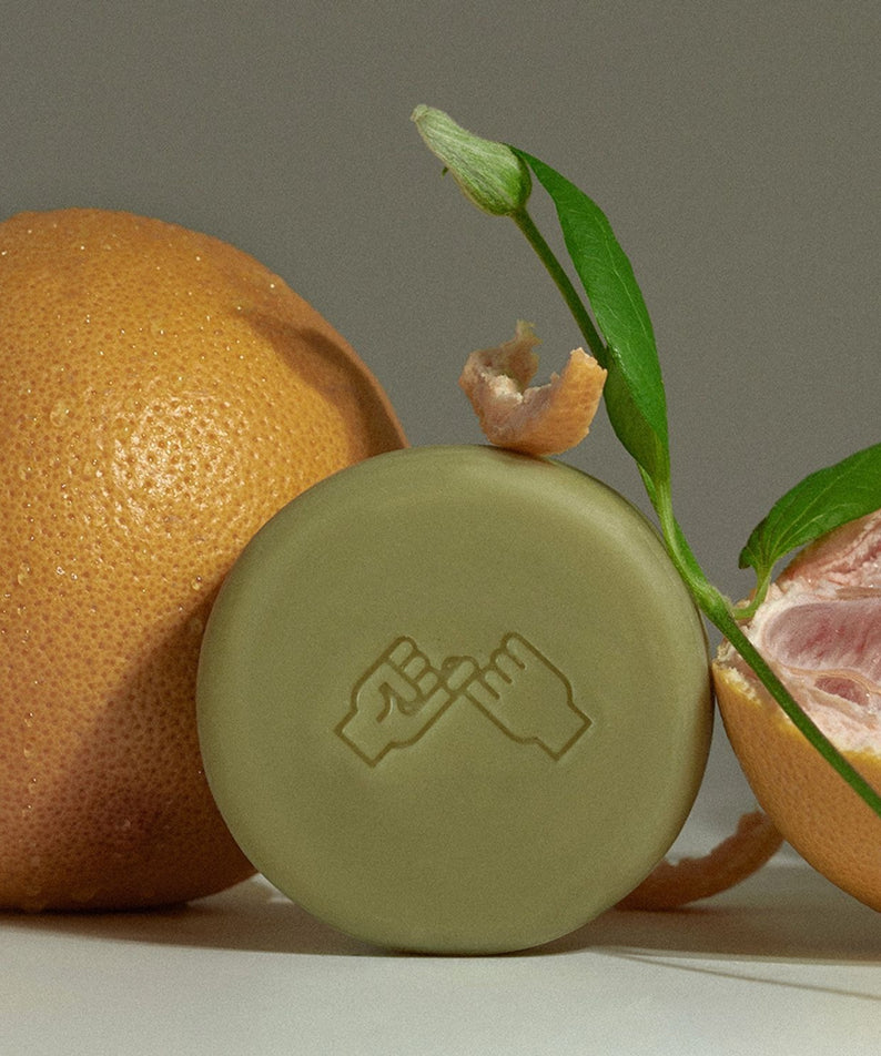 DONGGUBAT Correct Shampoo Bar For Dry Skin sur fond clair, entouré d’agrumes et de feuilles, marque DONGGUBAT.