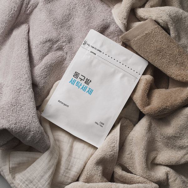 Décris l'image en français : DONGGUBAT Laundry Detergent 70 Tablets, marque DONGGUBAT, sachet sur linge beige.