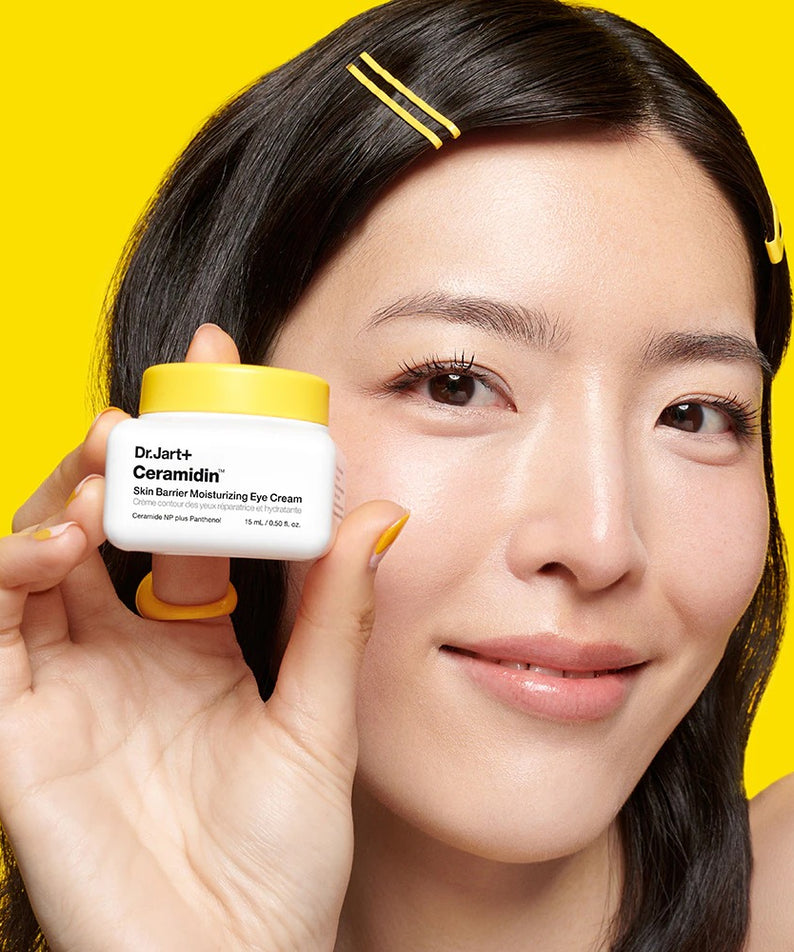 Femme souriante tenant DR.JART+ Ceramidin Skin Barrier Moisturizing Eye Cream 15ml devant un fond jaune.