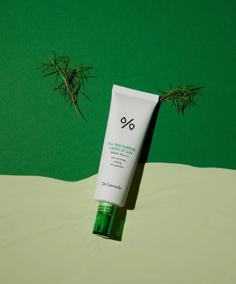 DR.CEURACLE Tea Tree Purifine Green Up Sun 50ml, tube sur fond vert et sable, décor thé vert et branches, marque visible.