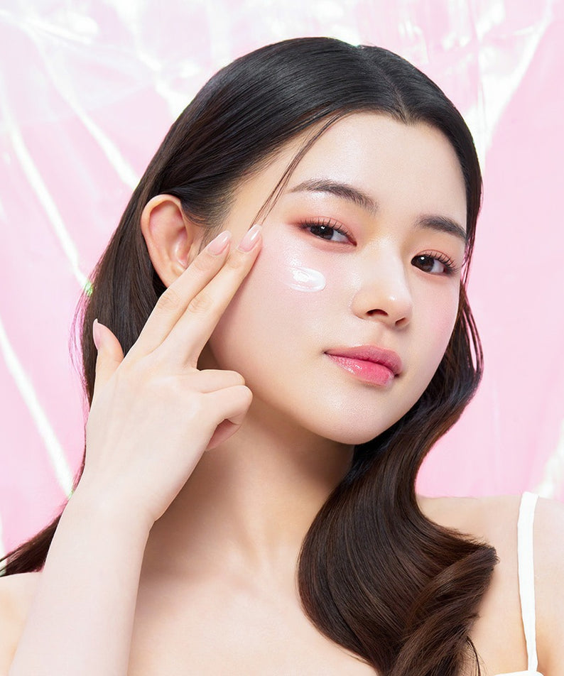 Femme appliquant EDIT.B Veil On Skin Boosthing Prep 50ml sur la joue pour une peau éclatante et hydratée, fond rose élégant en arrière-plan.